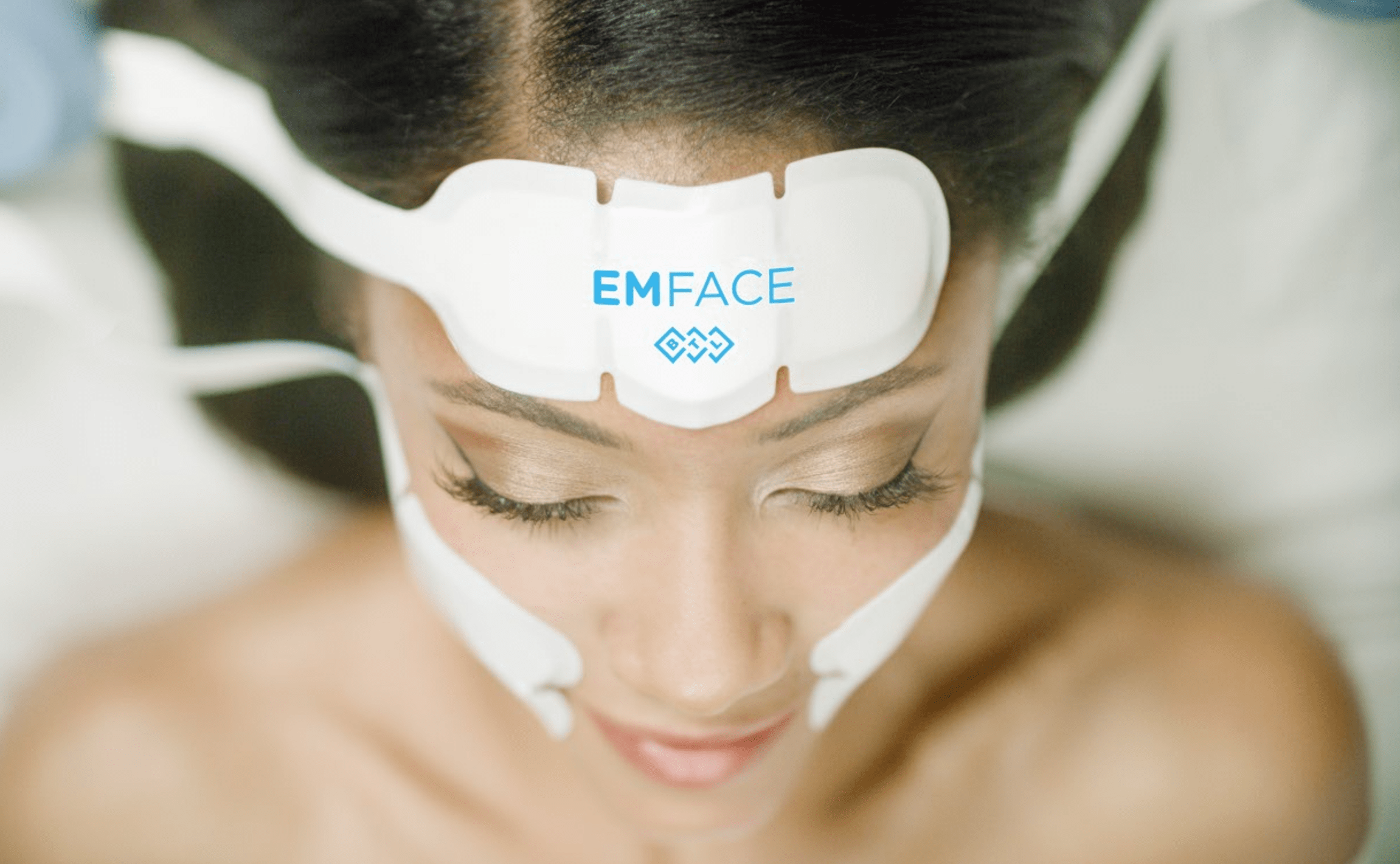 Woman receiving EMFACE facial treatment with electrodes on forehead and cheeks.