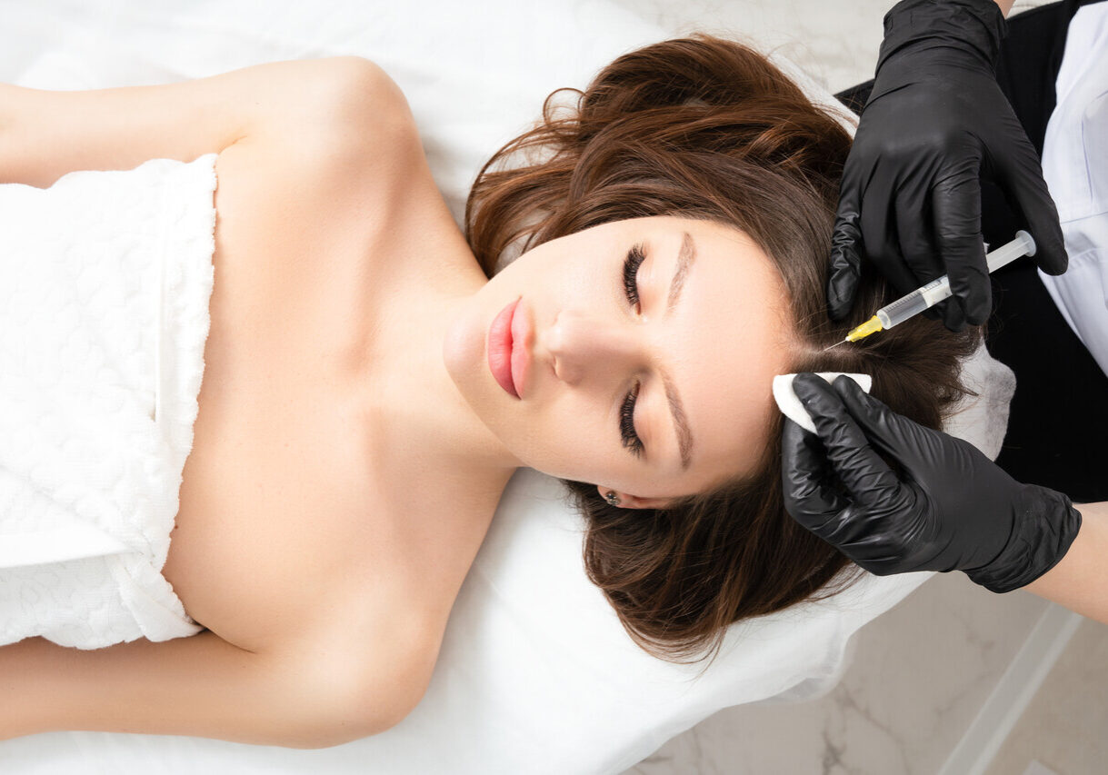 Mesotherapy,  vitamin injections in head skin of hair area. Professional hair loss treatment. Close up view of woman head and doctor's hands with syringe. View above.